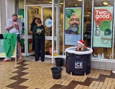 A woman dressed in an elf costume sits in an ice bath outside a Specsavers store for Icebreaker.