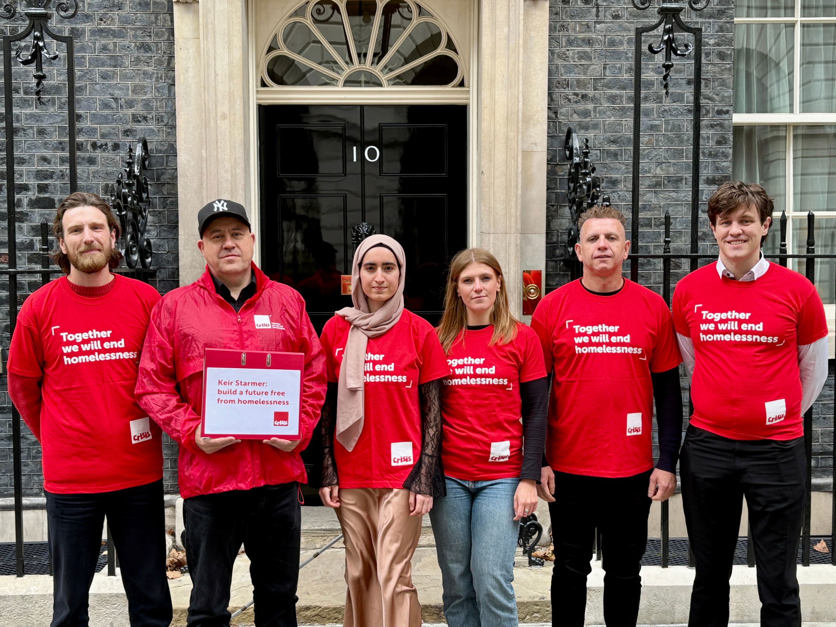 Six people wearing red Crisis t-shirts stand in front of the black door of Number 10 Downing Street,