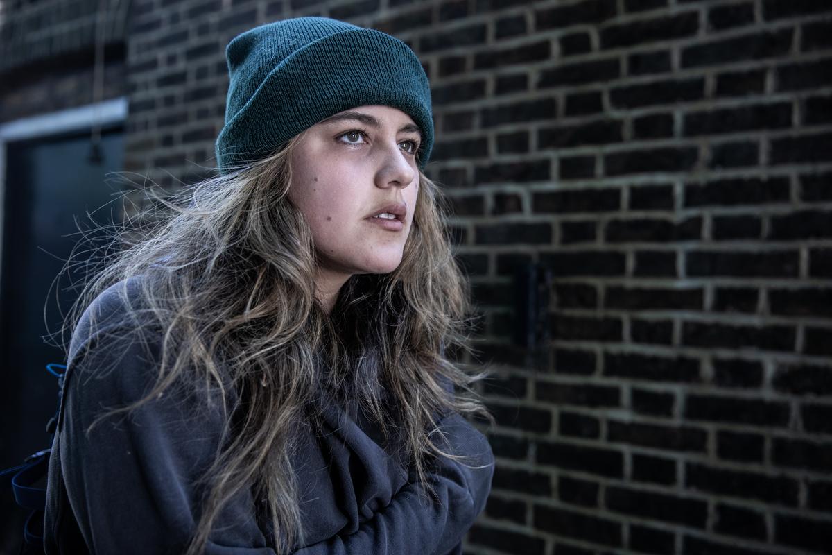 A white woman wearing a woolly hat standing in front of a brick wall